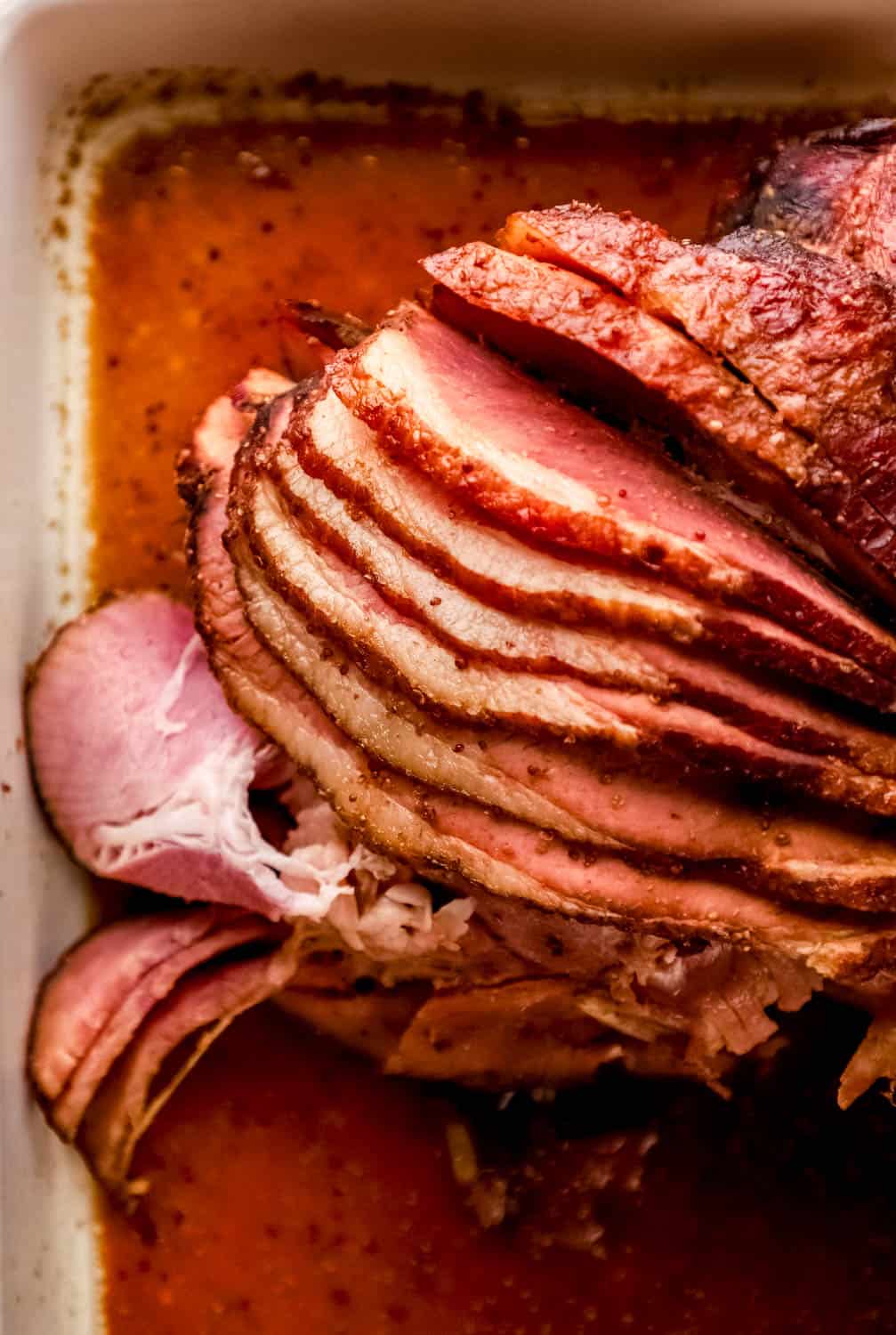 Overhead view of sliced ham covered in glaze in a white baking dish. 