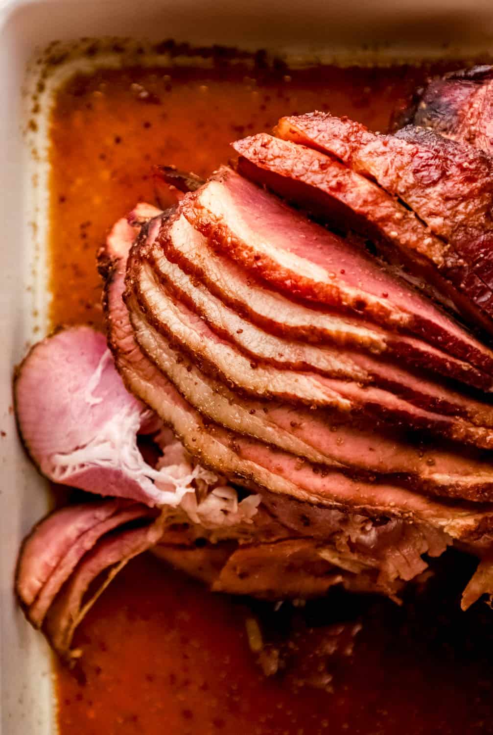 Overhead view of sliced ham covered in glaze in a white baking dish.