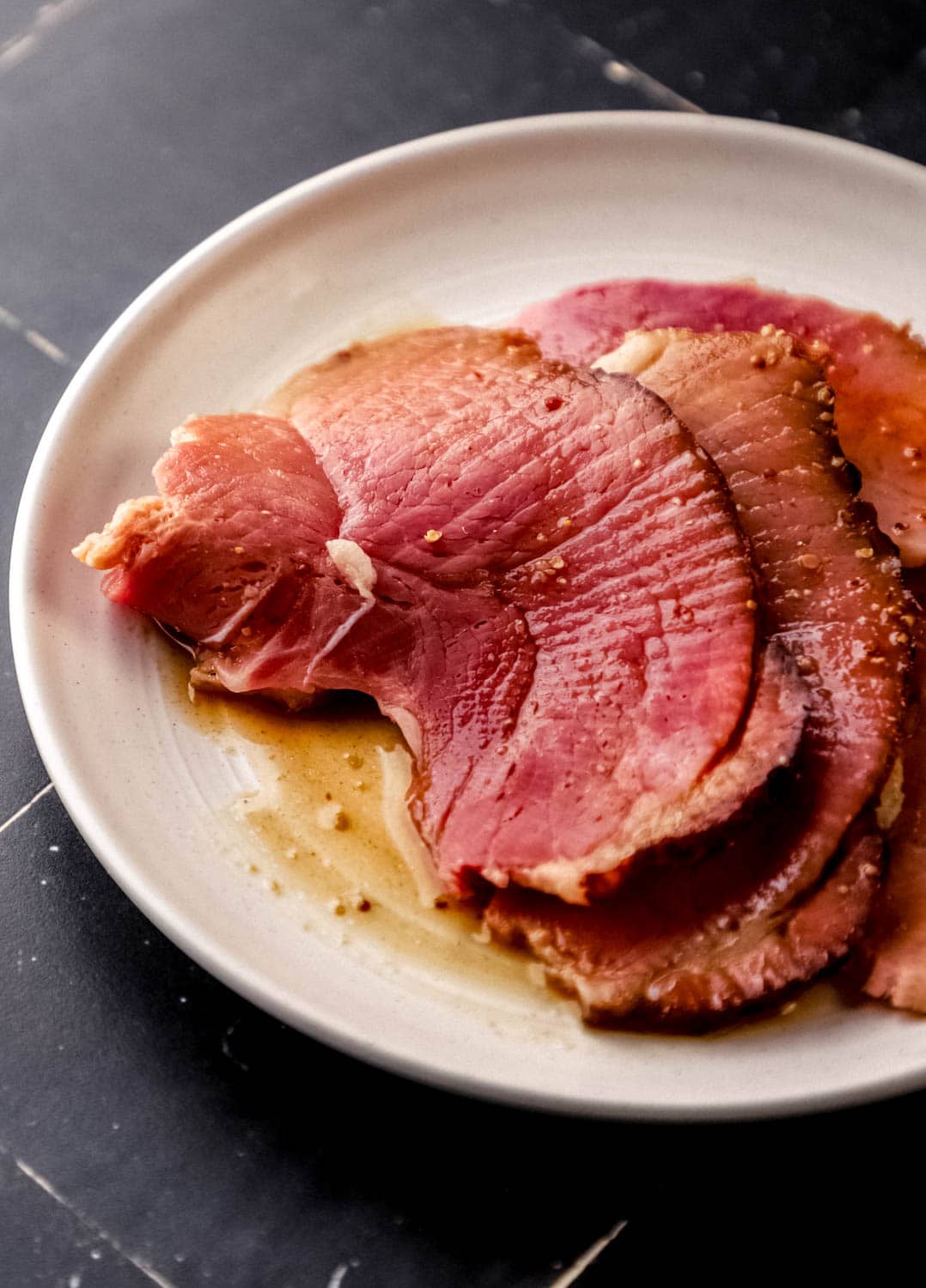 Close up side view of slices on ham covered in glaze on white plate.