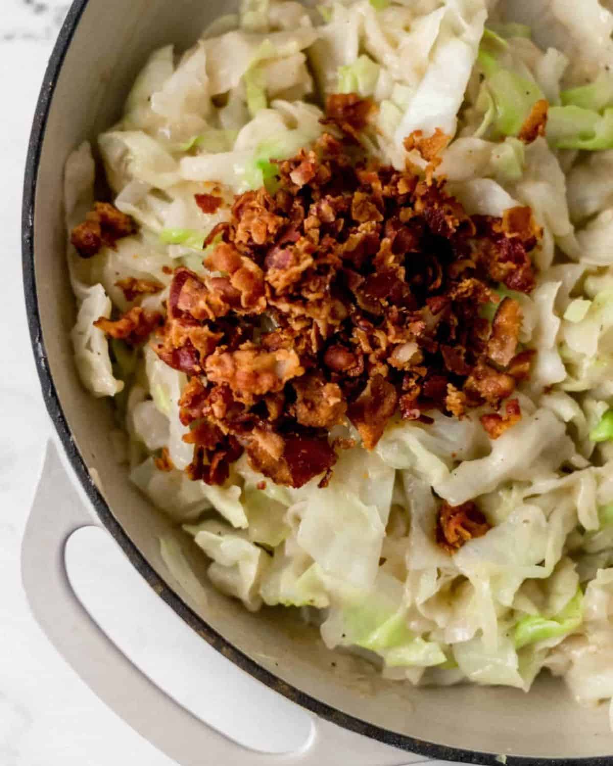 Bacon added to cabbage in large white braiser pan. 