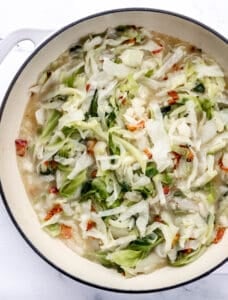 Overhead view of cabbage in large white braiser pan on marble surface.