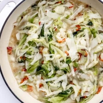 Overhead view of cabbage in large white braiser pan on marble surface.