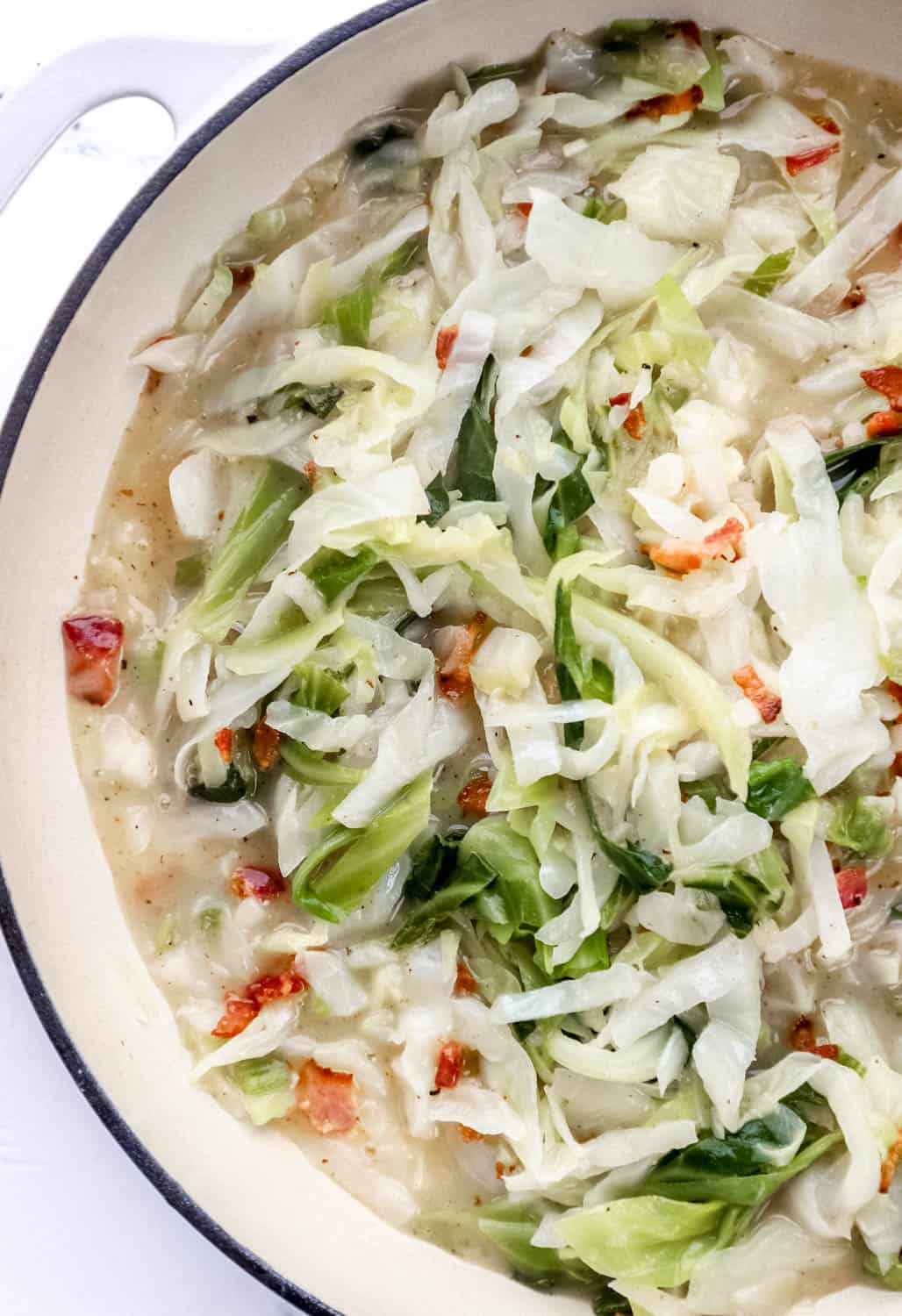 Finished sweet and sour cabbage combined with chopped bacon in large white braiser pan. 