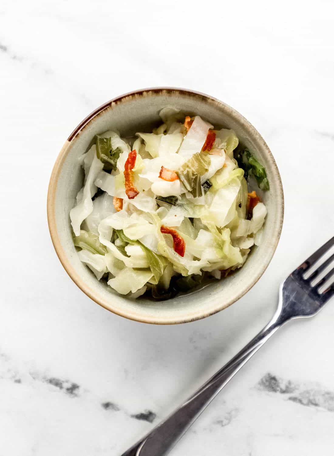 Small bowl with single serving of cabbage in it beside a fork. 