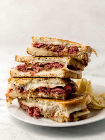 Close up side view of two grilled cheese sandwiches stacked on top of each other on white plate with chips on it.