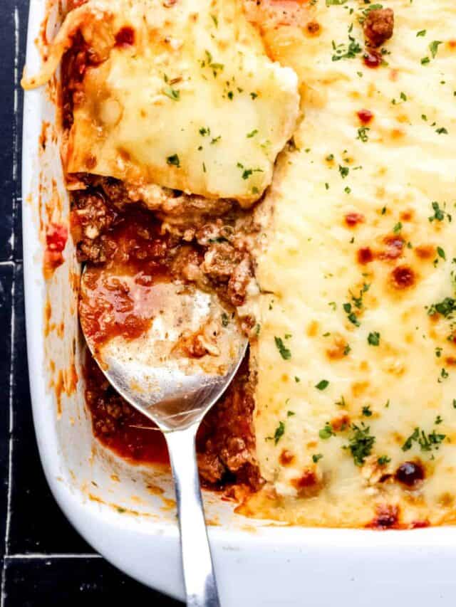 Overhead view of lasagna in white baking dish with serving spoon in it.