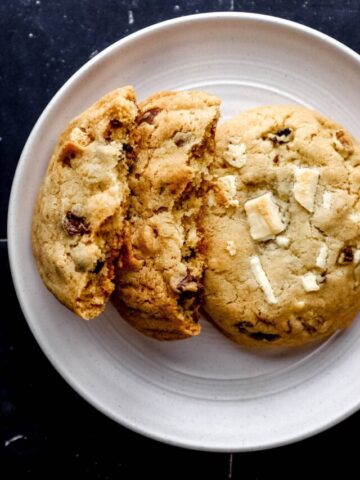 Overhead view of two cookies on white plate with one cookie broke in half.