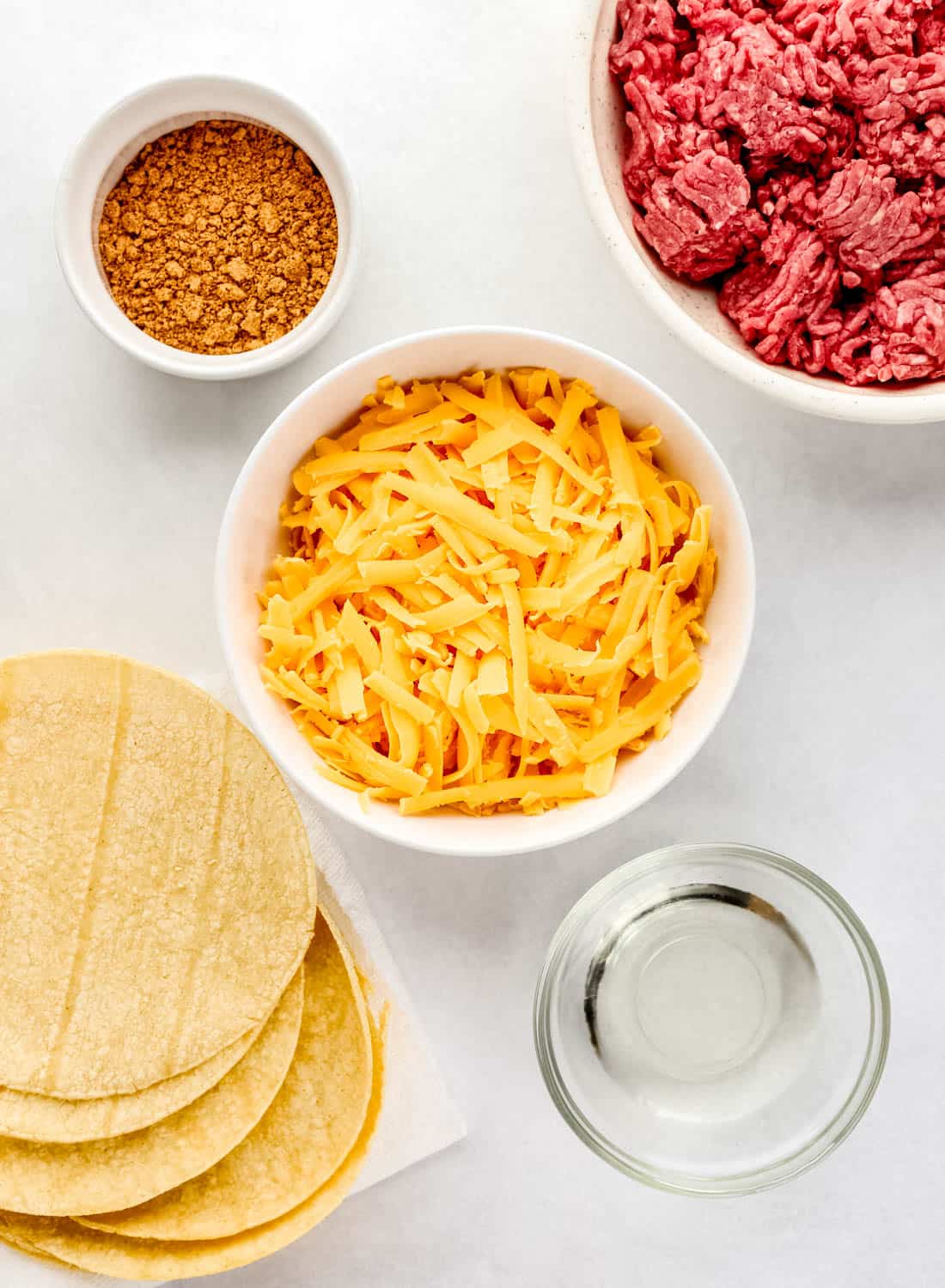 Overhead view of ingredients needed to make tacos in separate bowls on white surface. 