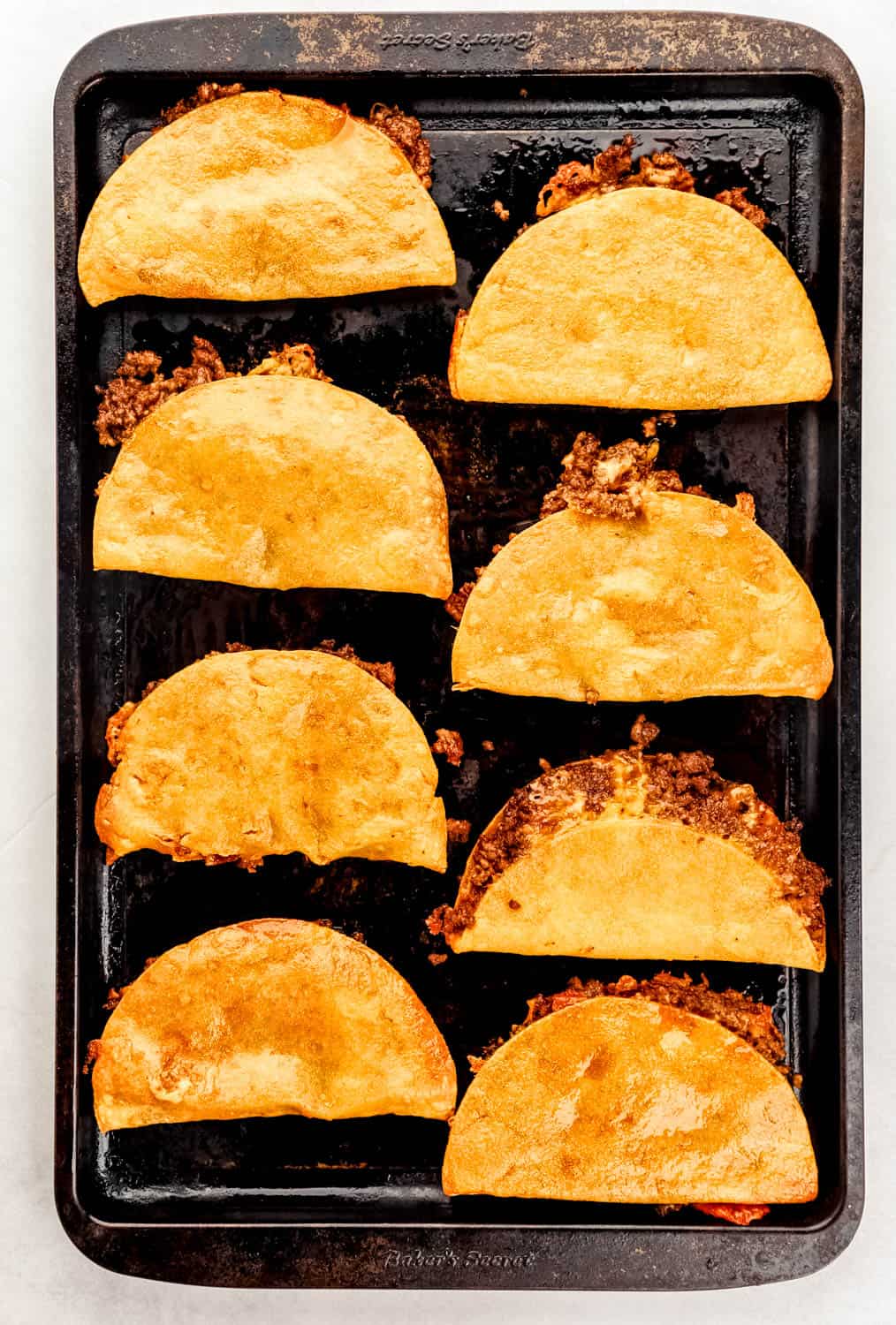 Overhead view of baked beef and cheese tacos on baking sheet. 
