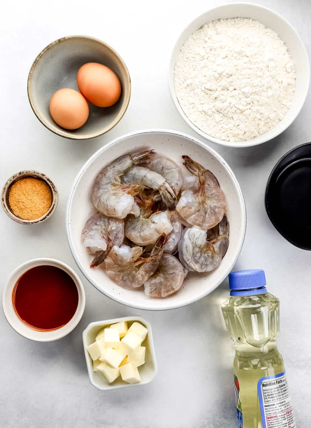 Overhead view of ingredients needed to make shrimp in separate bowls on white surface. 