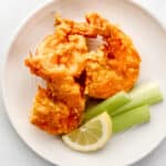 Three shrimp on white plate with celery sticks and lemon slices.