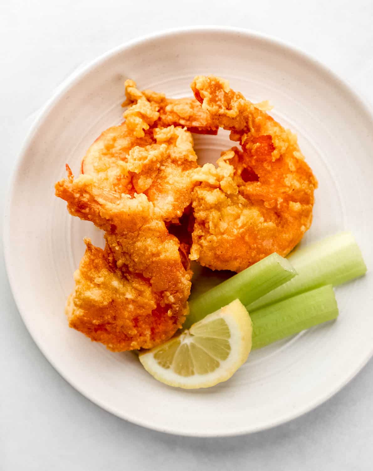 Three finished shrimp on white plate with celery sticks and a lemon slice. 