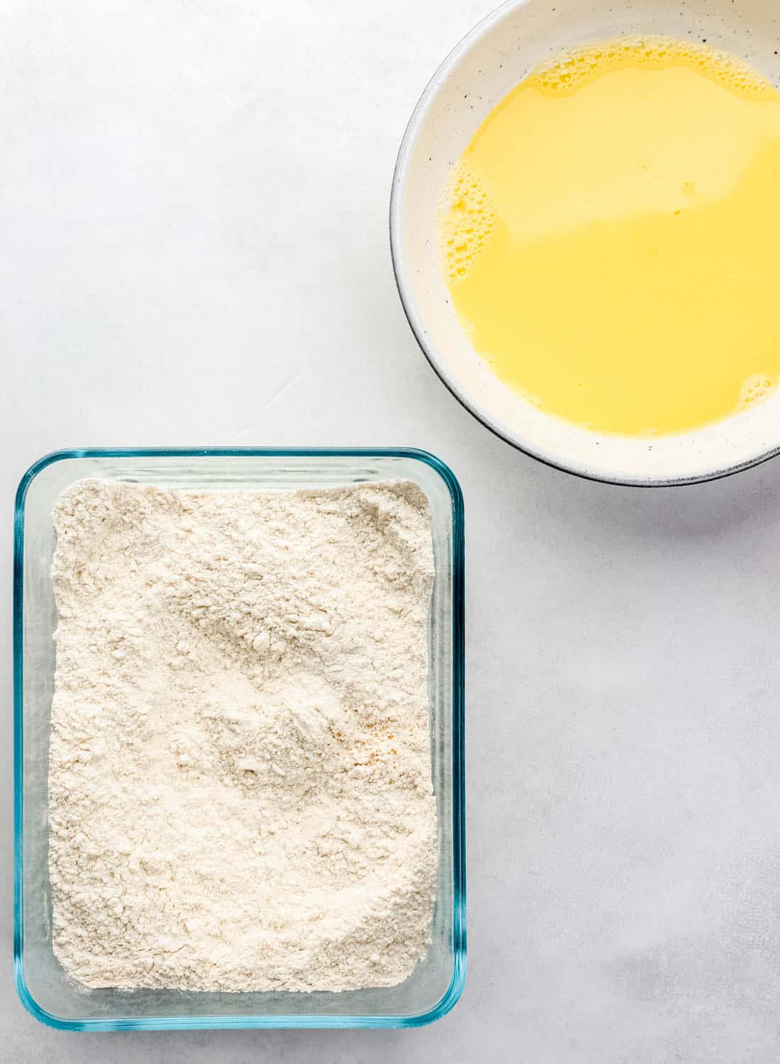 Flour mixture in a rectangle glass container and egg mixture in a white bowl. 