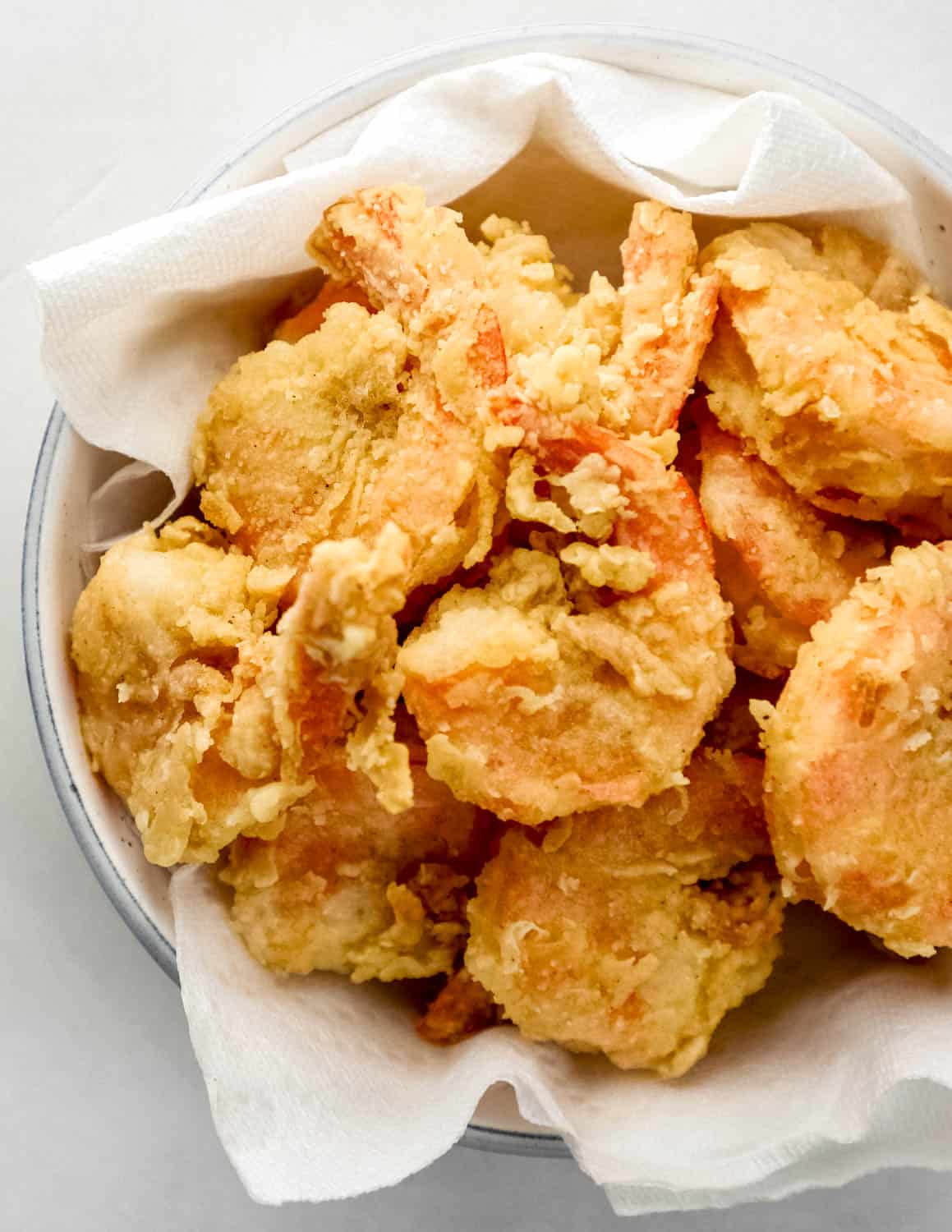 Crispy fried shrimp in white paper towel lined bowl. 