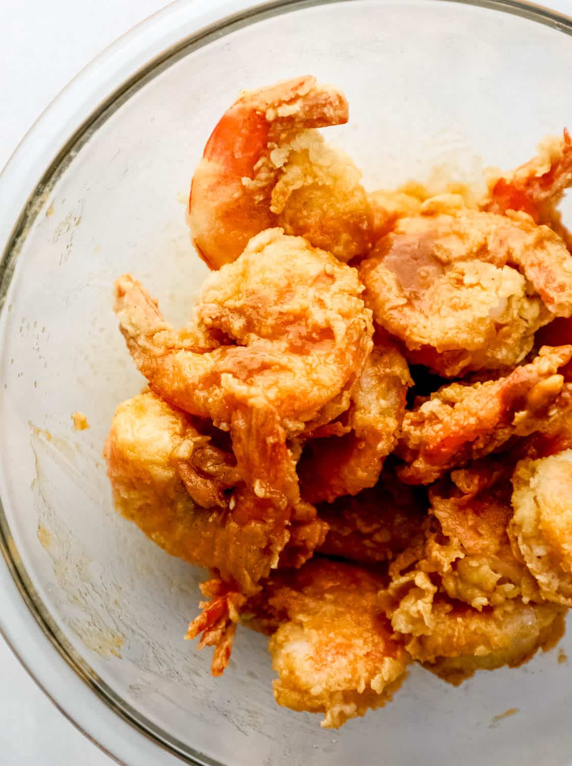 Shrimp tossed in buffalo sauce in large glass mixing bowl. 