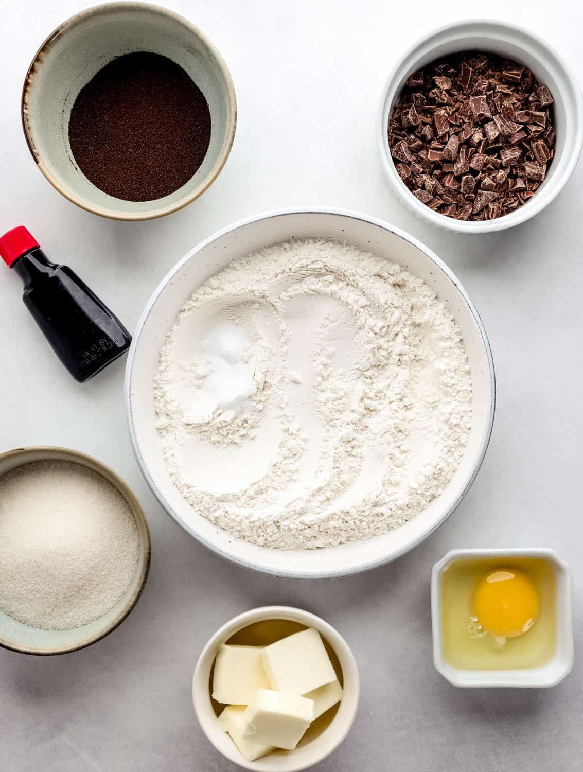 Overhead view of ingredients needed to make cookies in separate bowls on white surface. 