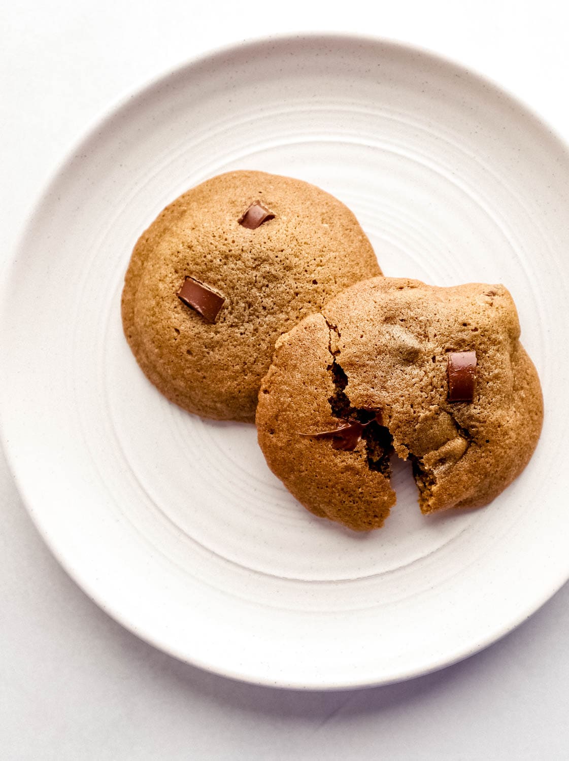 Two baked cookies on white plate with one of the cookies broke in half. 