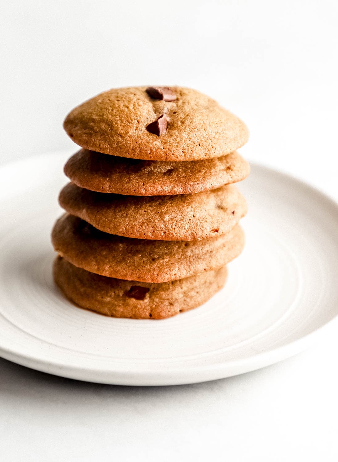 Close up side view of cookies stacked on top of each other on a white plate. 