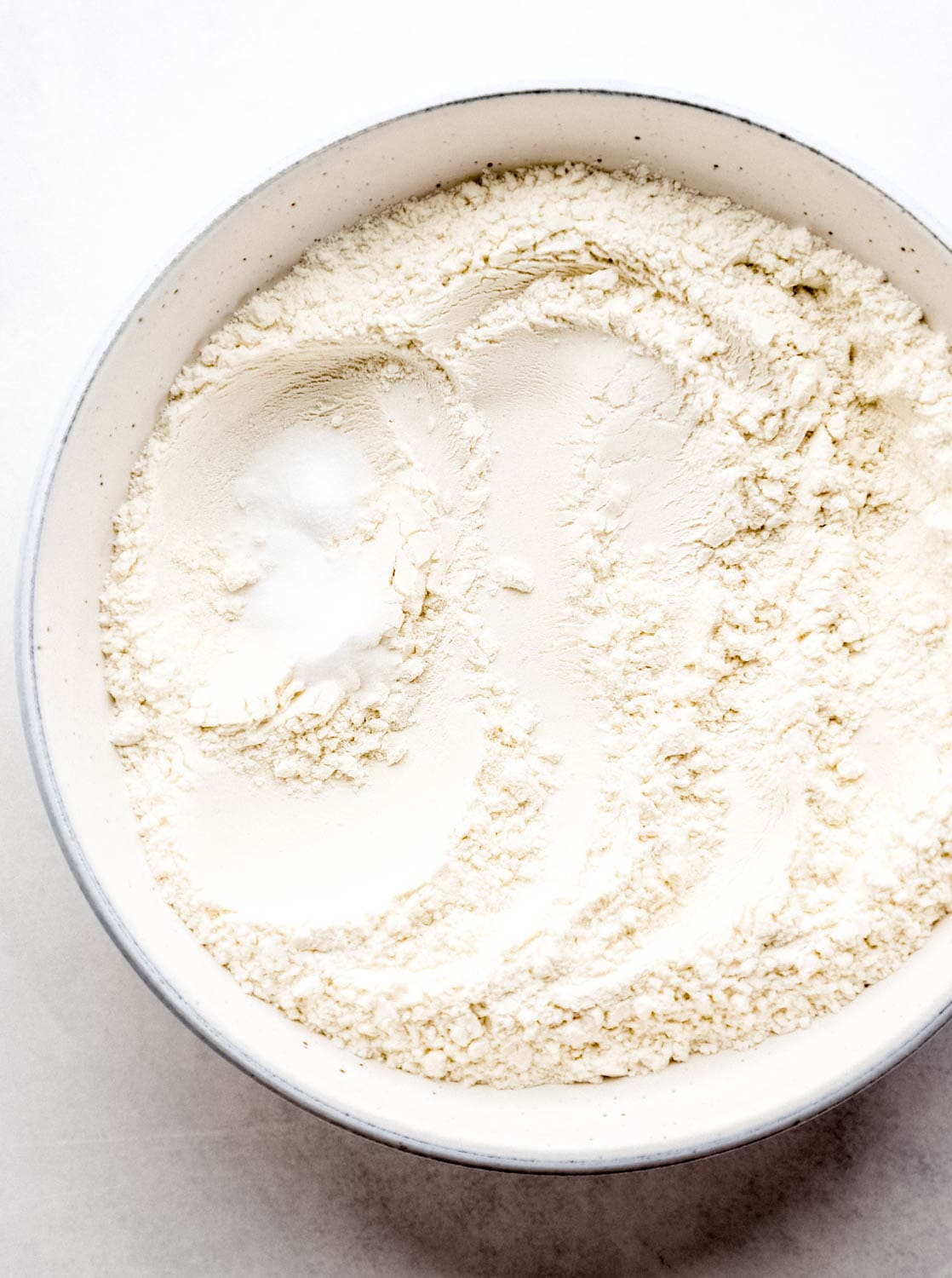 Overhead view of flour, salt, and baking soda in white bowl. 