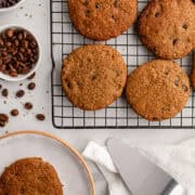 Baked cookies on a baking rack by a cookie on a plate.