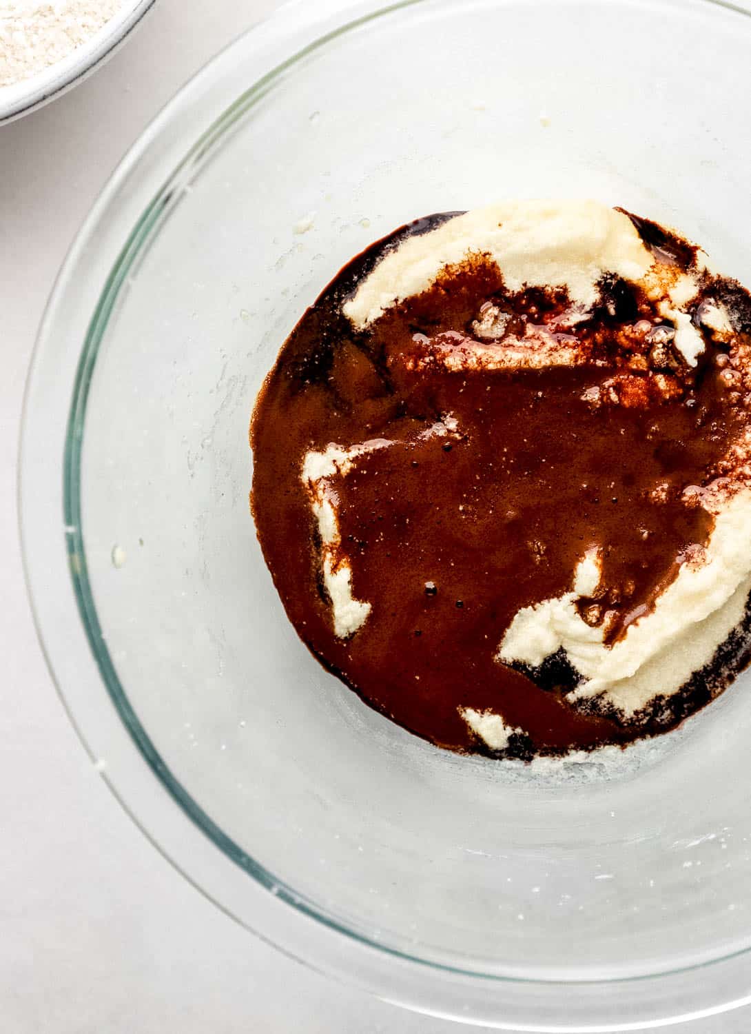 Espresso mixture added to the other wet ingredients in a large glass mixing bowl on white surface. 