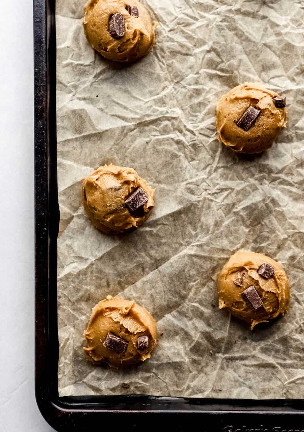 Cookie dough scooped onto a parchement lined baking sheet before baking. 