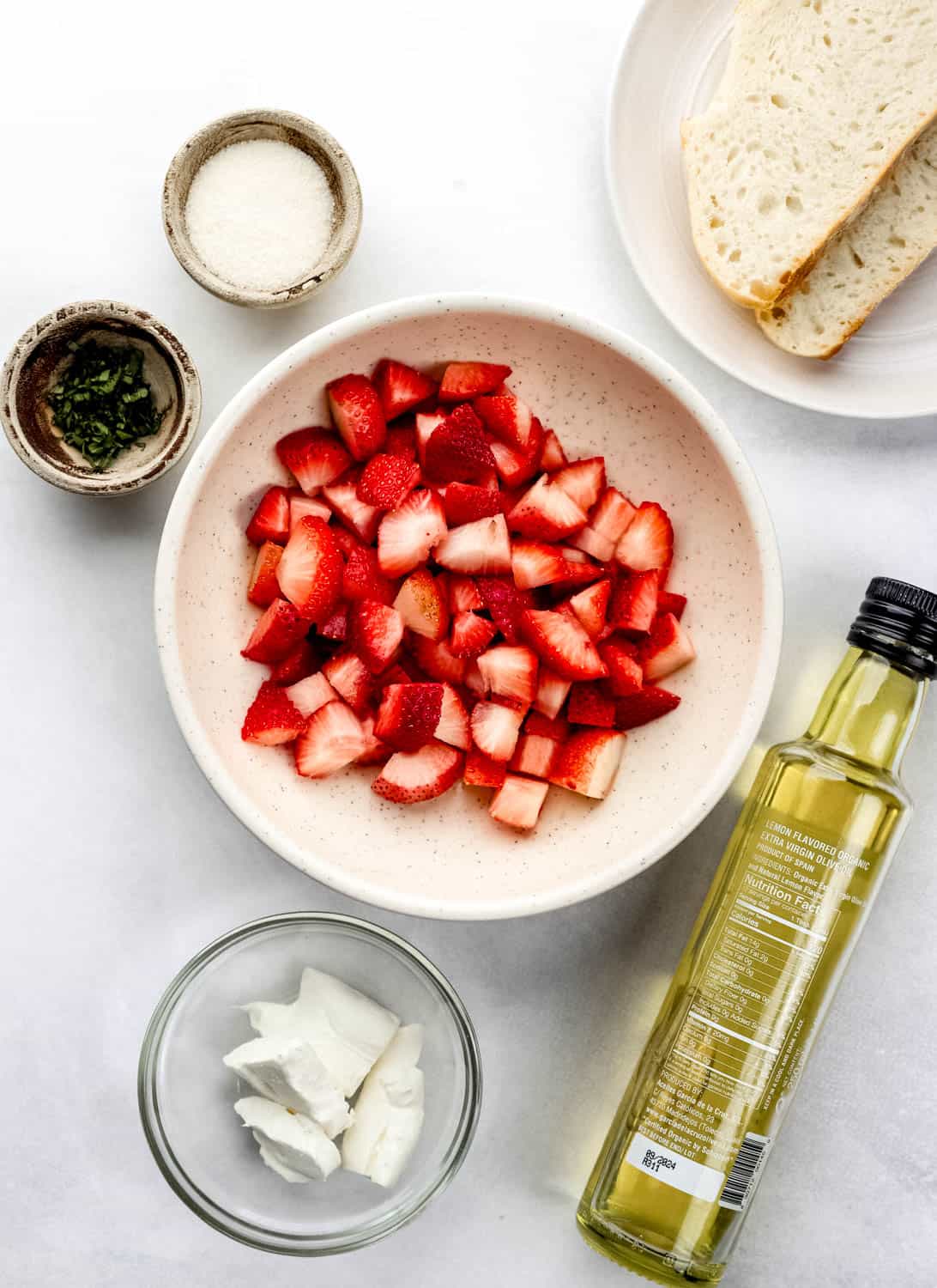 Overhead view of ingredients needed to make toast in separate bowls on white surface. 