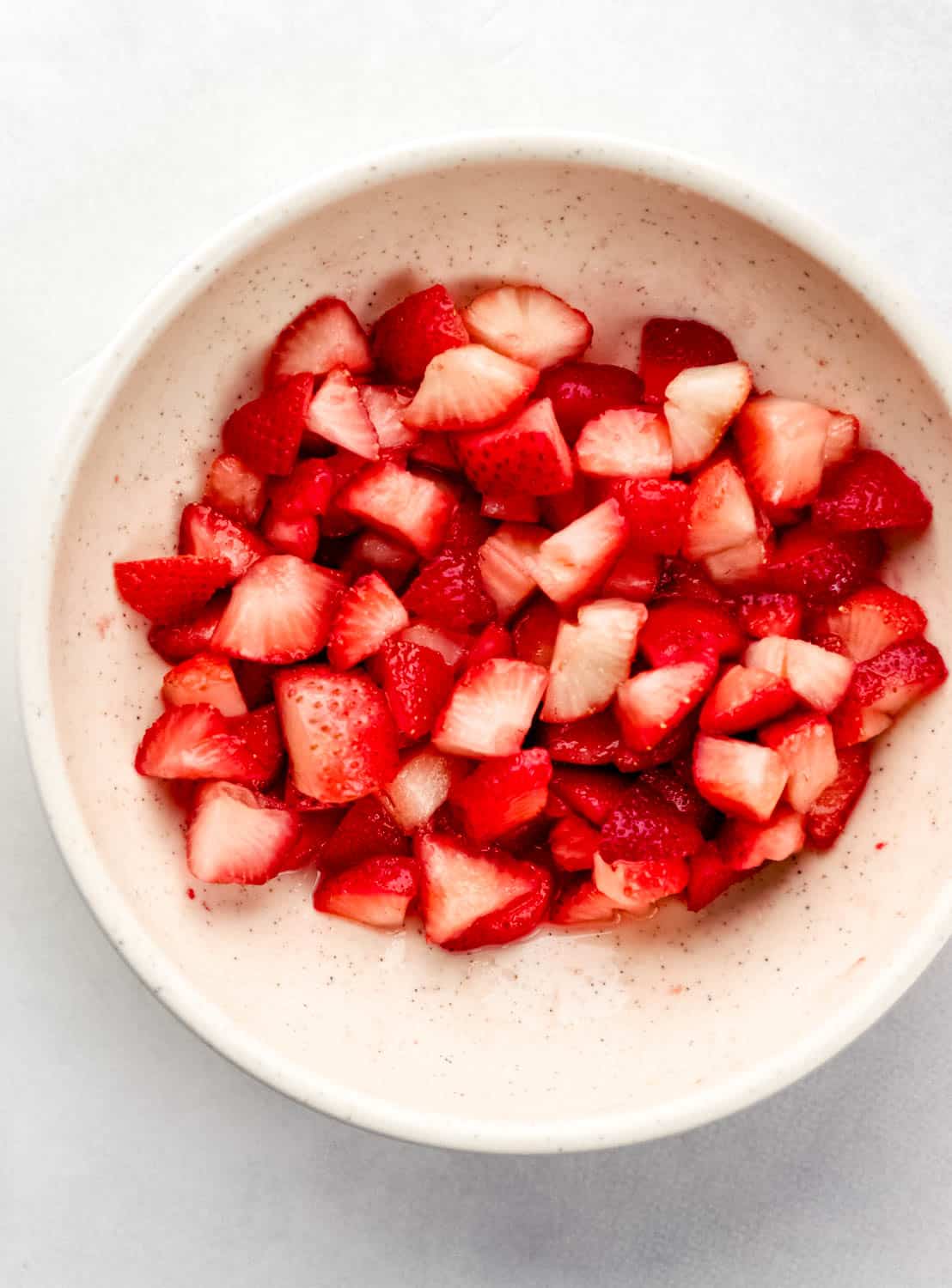Overhead view of quartered strawberries and sugar combined in white bowl. 
