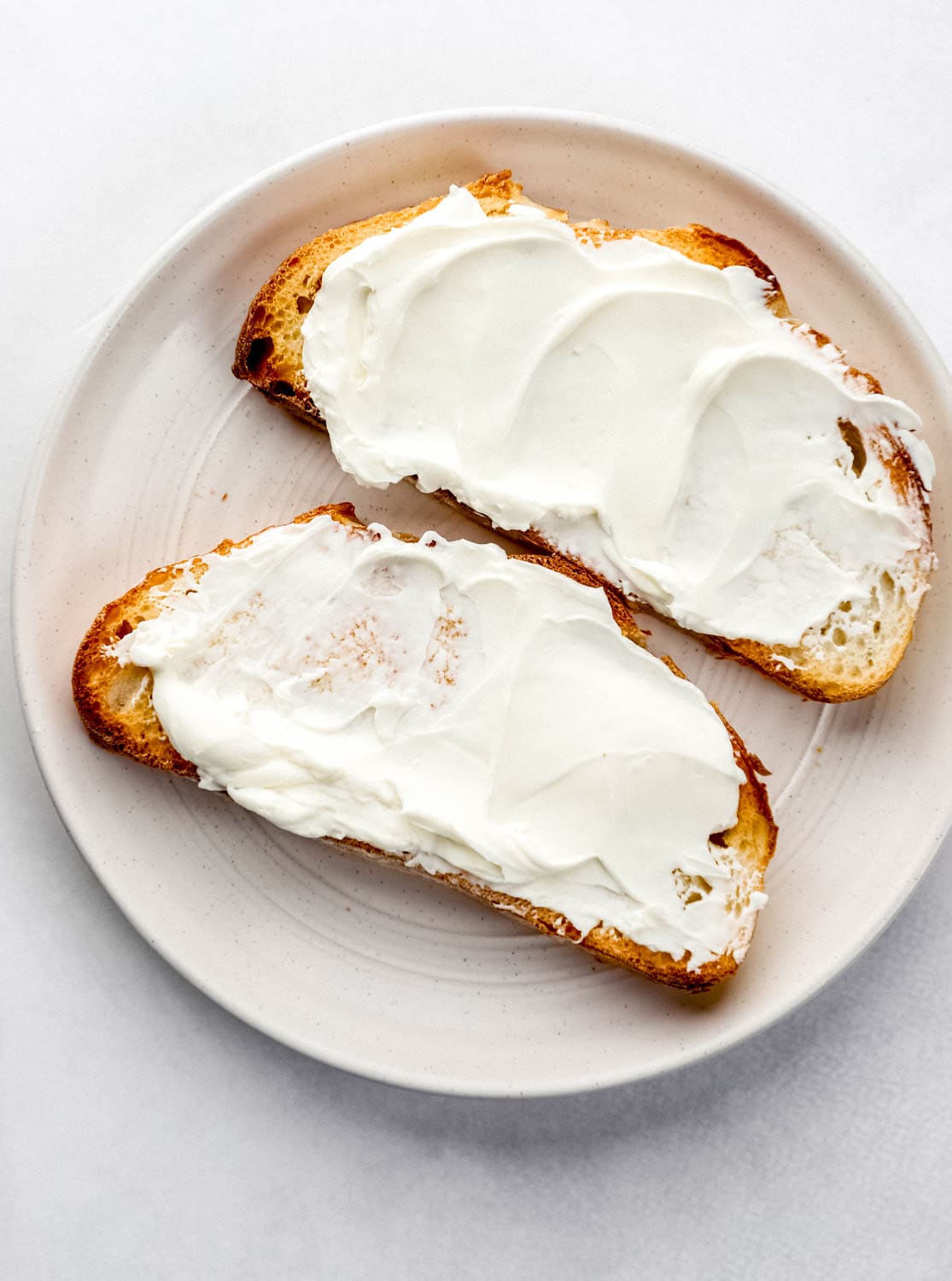 Two slices of cream cheese toast on white plate. 