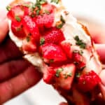 Hands holding strawberry cream cheese toast.