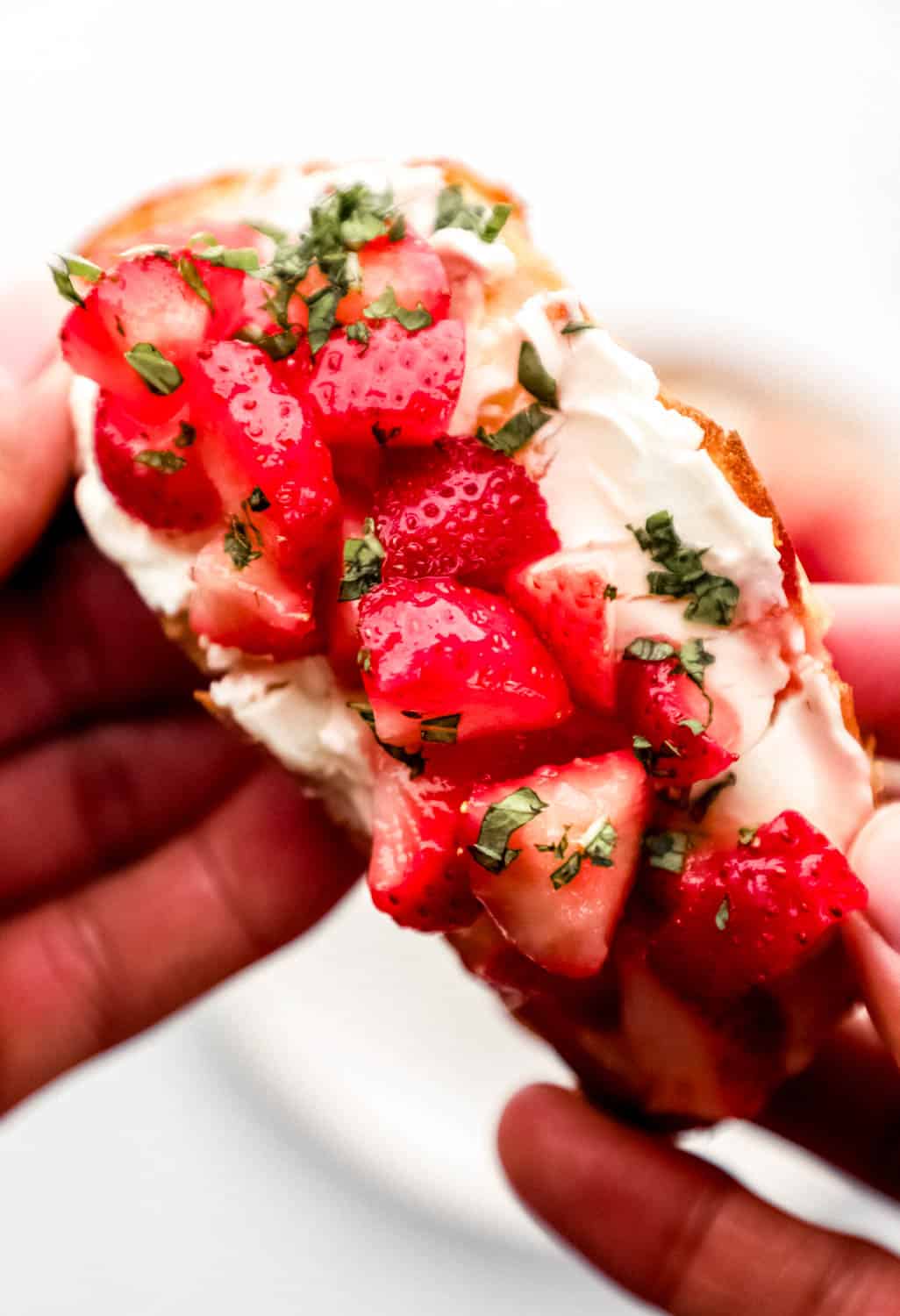 Hand holding slice of strawberry cream cheese toast. 