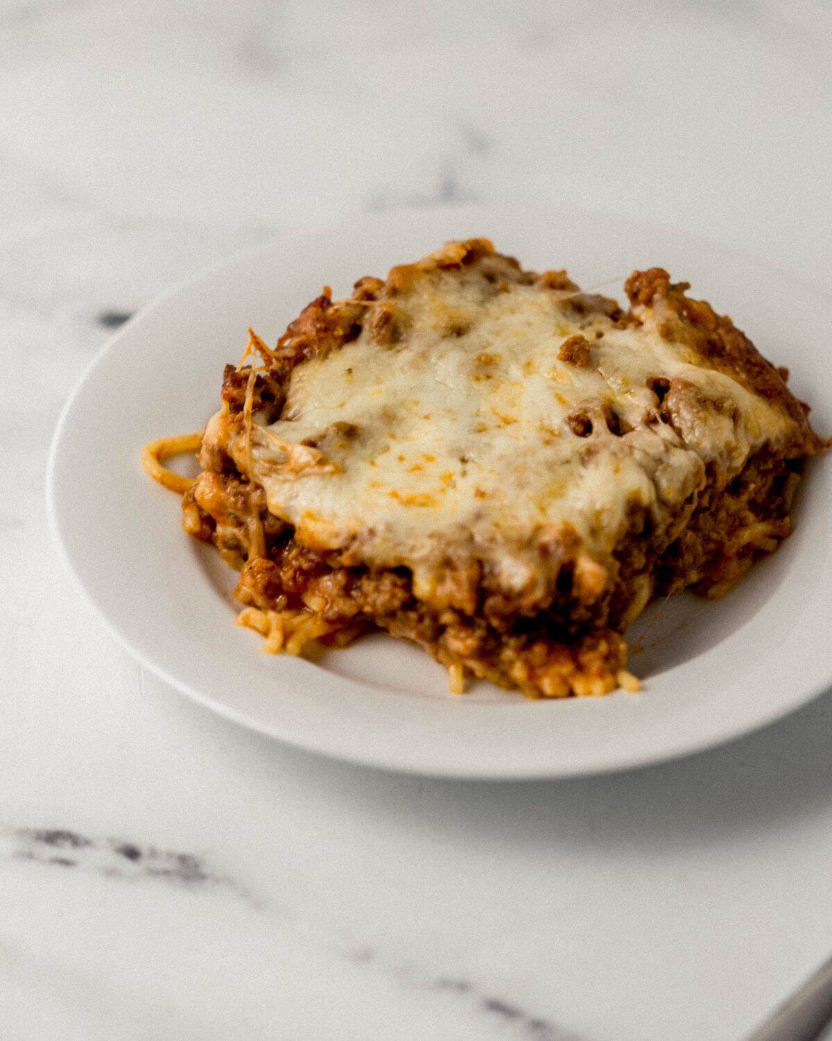 Close up front view of white plate with spaghetti on it on marble surface. 