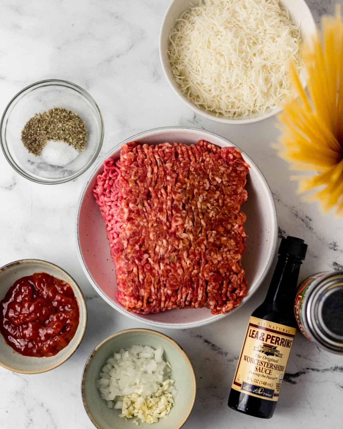 Overhead view of ingredients needed to make spaghetti in separate bowls on marble surface. 