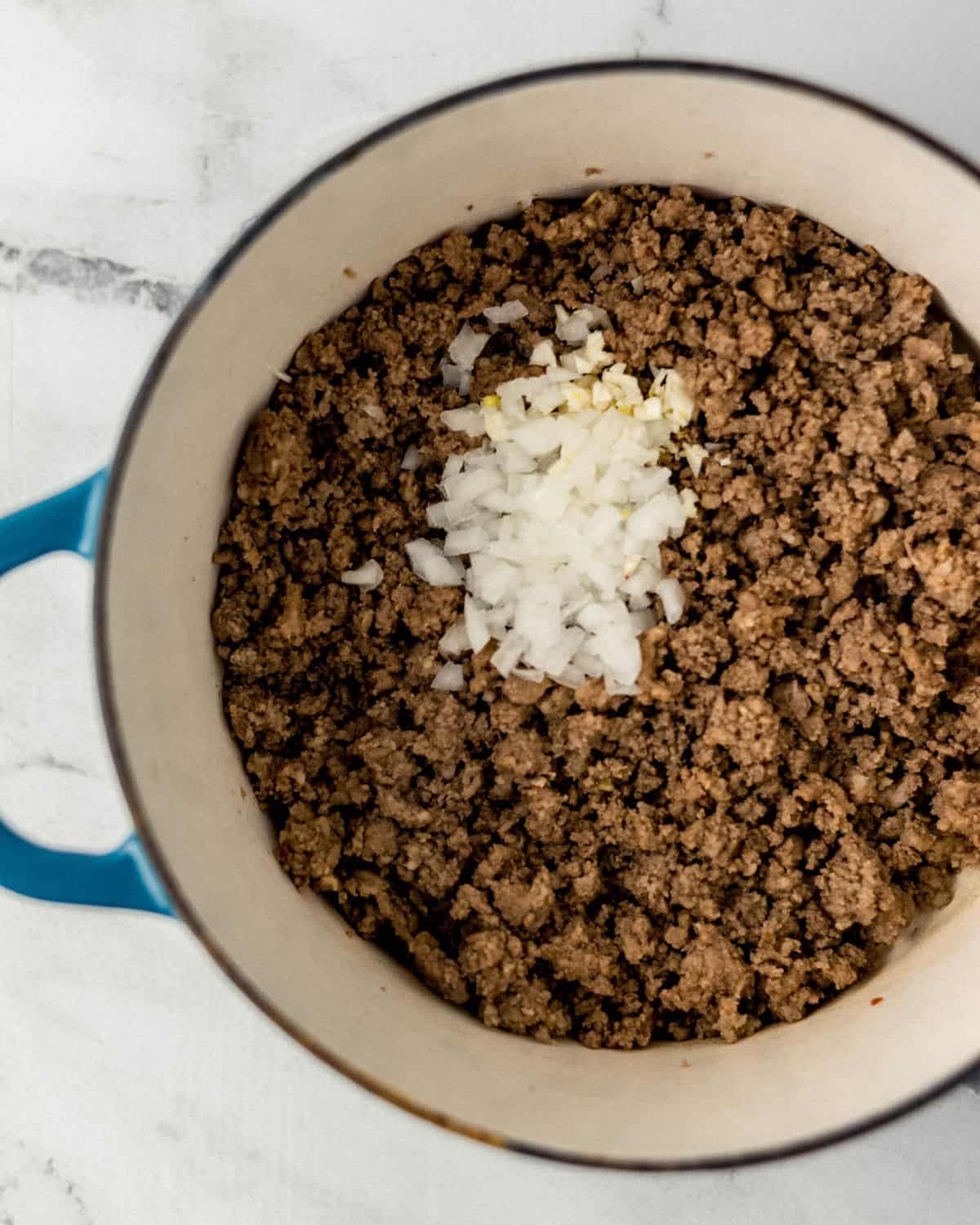 Overhead view of large pot with ground meat, onion, and garlic in it. 