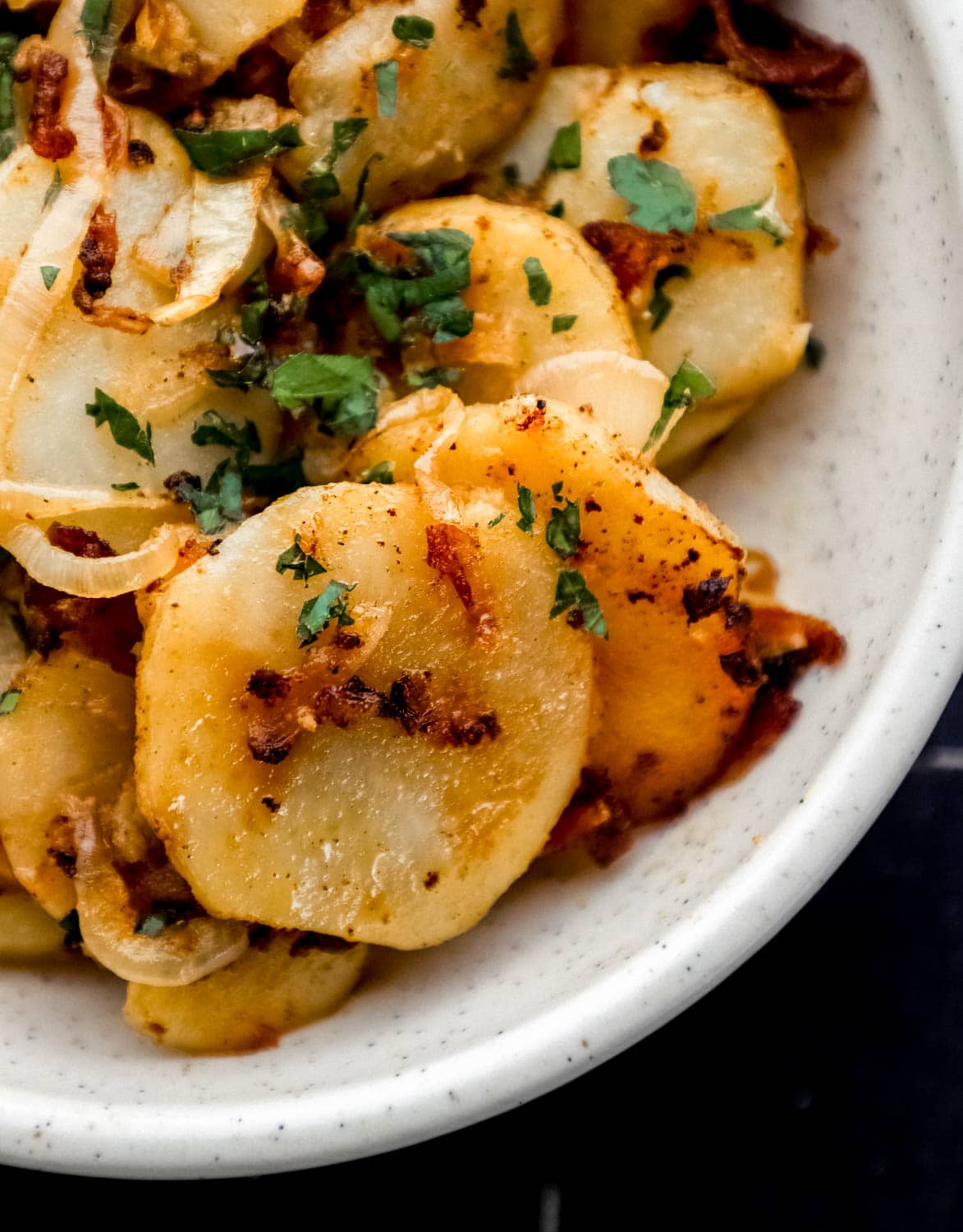 Close up view of finished potatoes in white bowl topped with chopped parsley. 