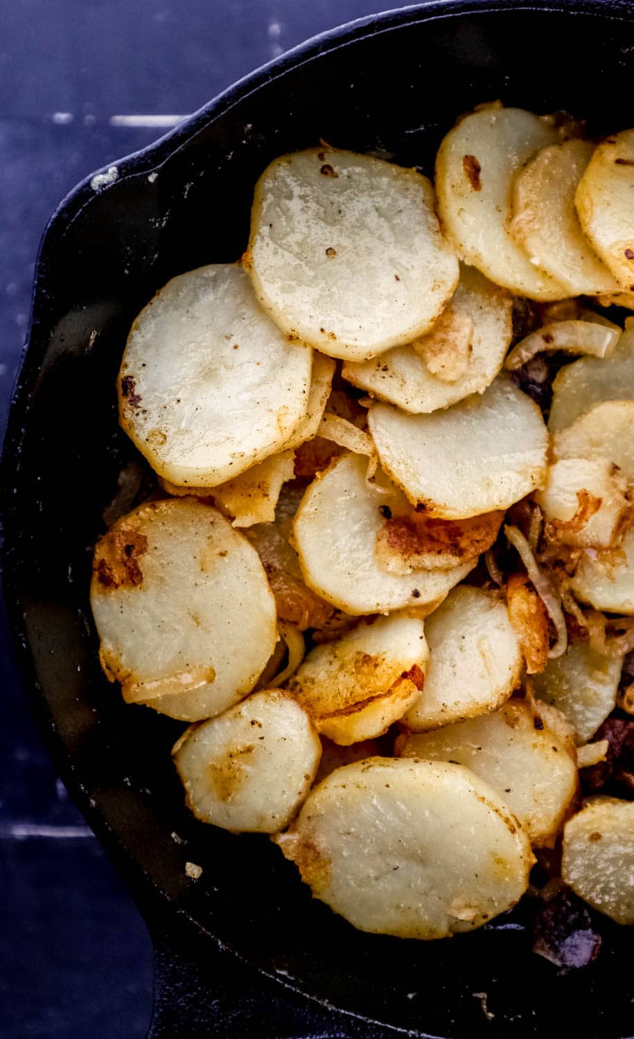 Close up view of potatoes cooking in a cast iron skillet.