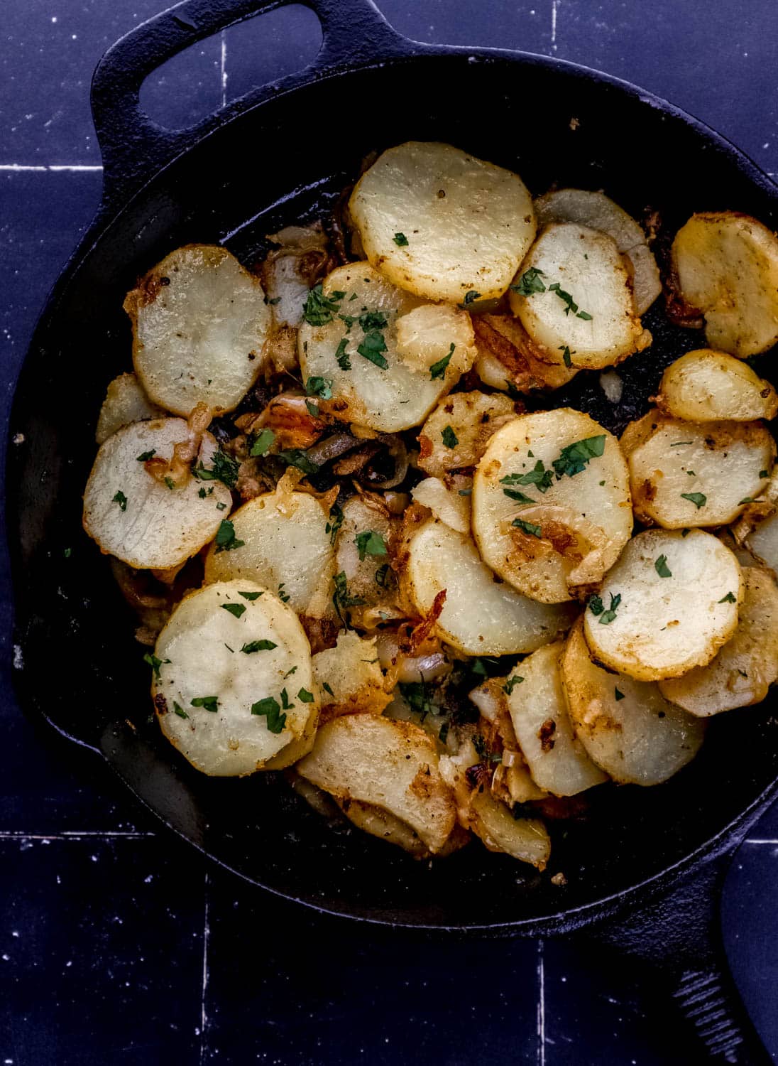 Overhead view of potatoes in cast iron skillet on black tile surface. 