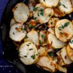 Close up overhead view of potatoes in cast iron skillet topped with chopped parsley.