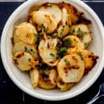 Overhead view of white bowl with finished potatoes in it by a fork.