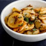 Close up front view of finished potatoes in white bowl on black tile surface.