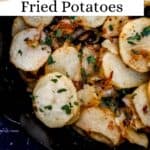 Close up overhead view of potatoes in cast iron skillet topped with parsley pin with text overlay.