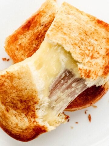 Overhead view of cheese sandwich pulled apart on white plate.