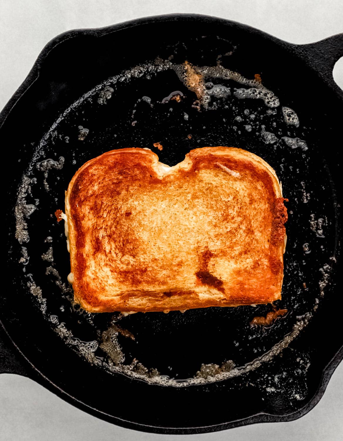 Overhead view of finished sandwich in cast iron skillet with melted butter in it. 