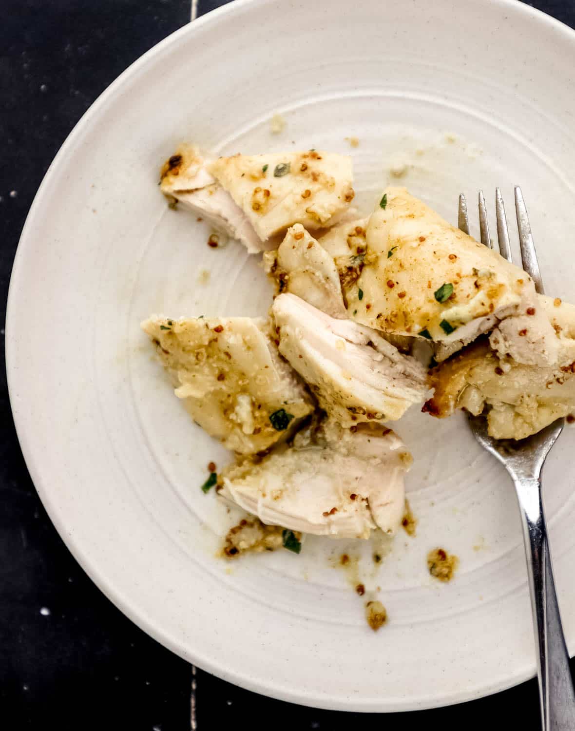 Piece of chicken on white plate with fork in it. 