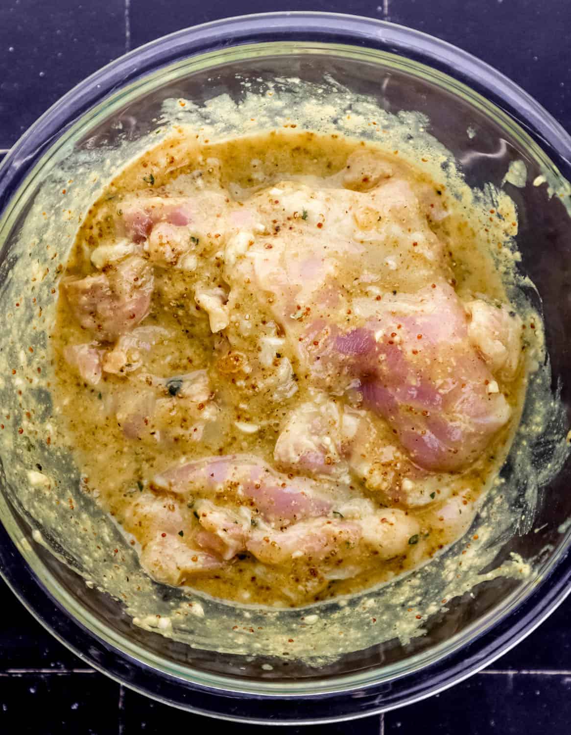Overhead view of marinade ingredients and chicken combined in large glass mixing bowl. 