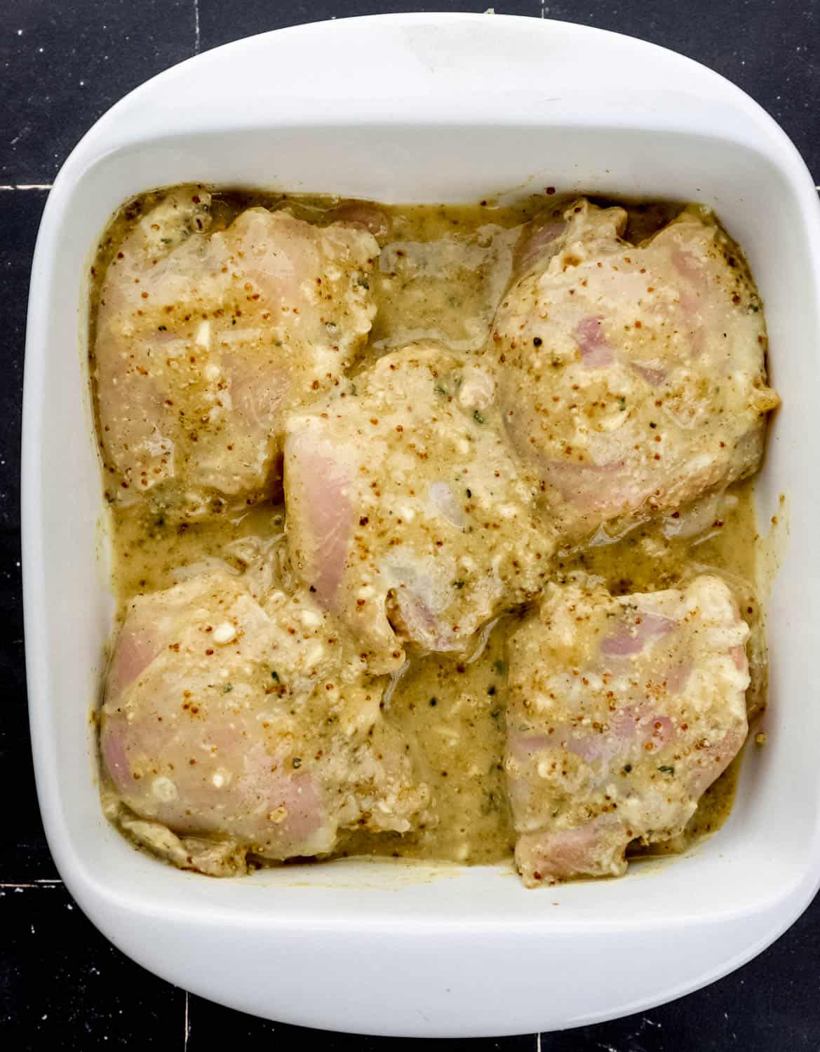 Overhead view of marinade and chicken in square white baking dish. 
