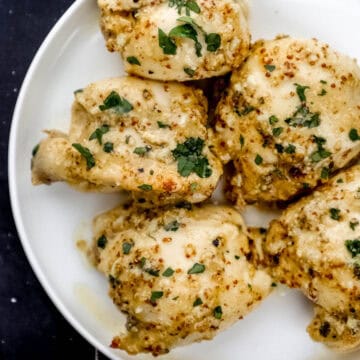 Overhead view of white plate of chicken topped with chopped parsley.