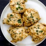 Overhead view of baked chicken on white plate on black tile surface.