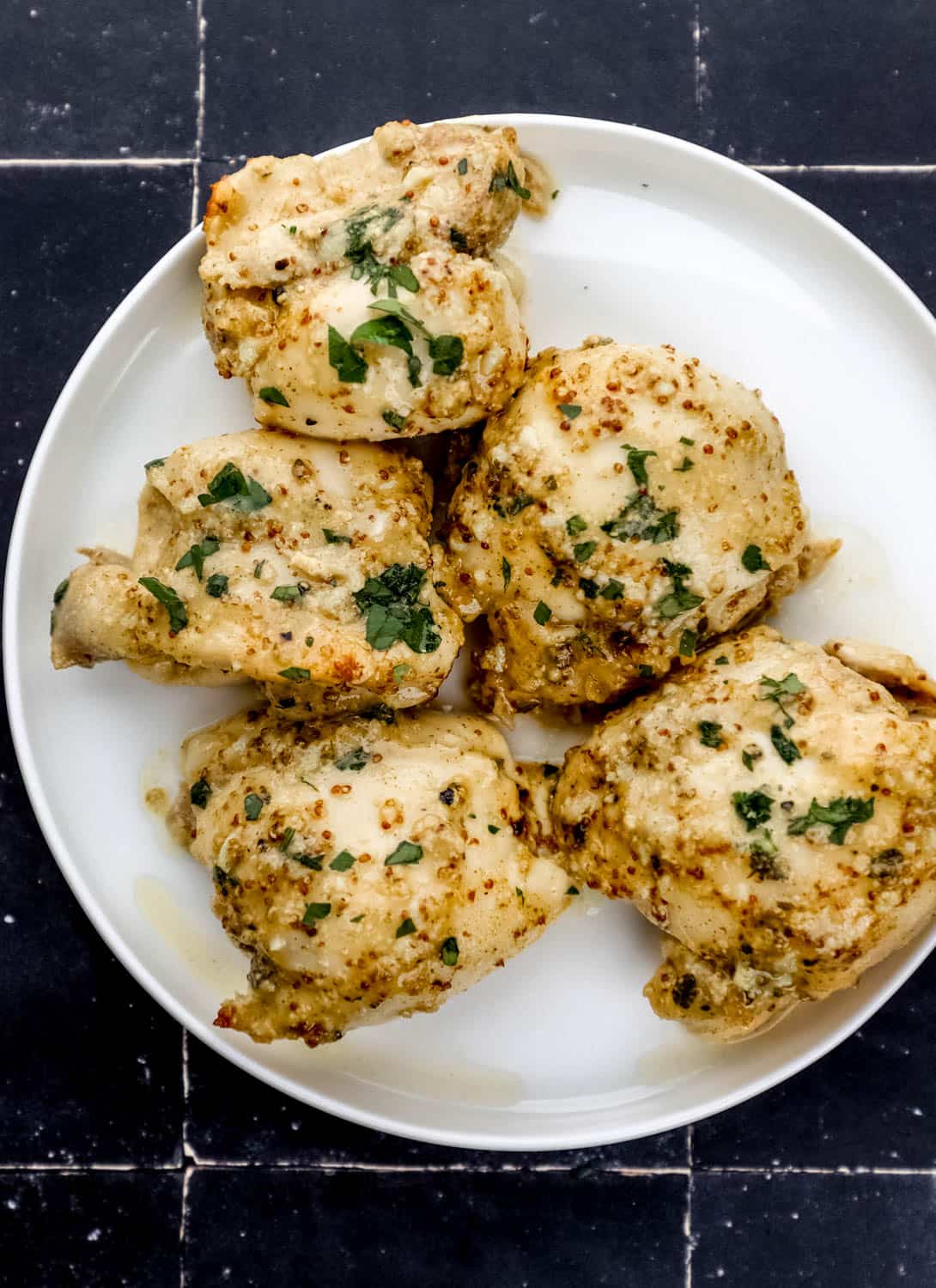 Overhead view of cooked chicken on white plate on black tile surface. 