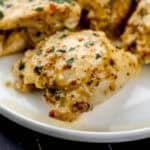 Close up front view of chicken on white plate topped with chopped parsley.